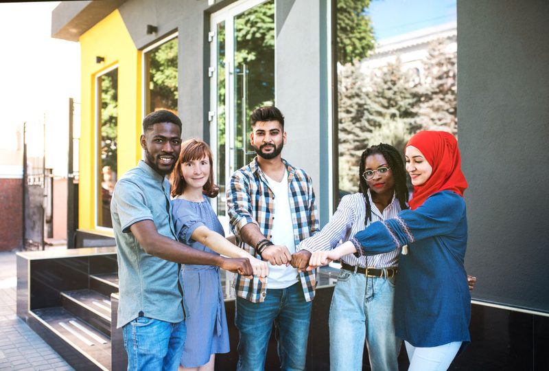 Fünf junge Menschen unterschiedlicher Herkunft stoßen gemeinsam die Fäuste zusammen